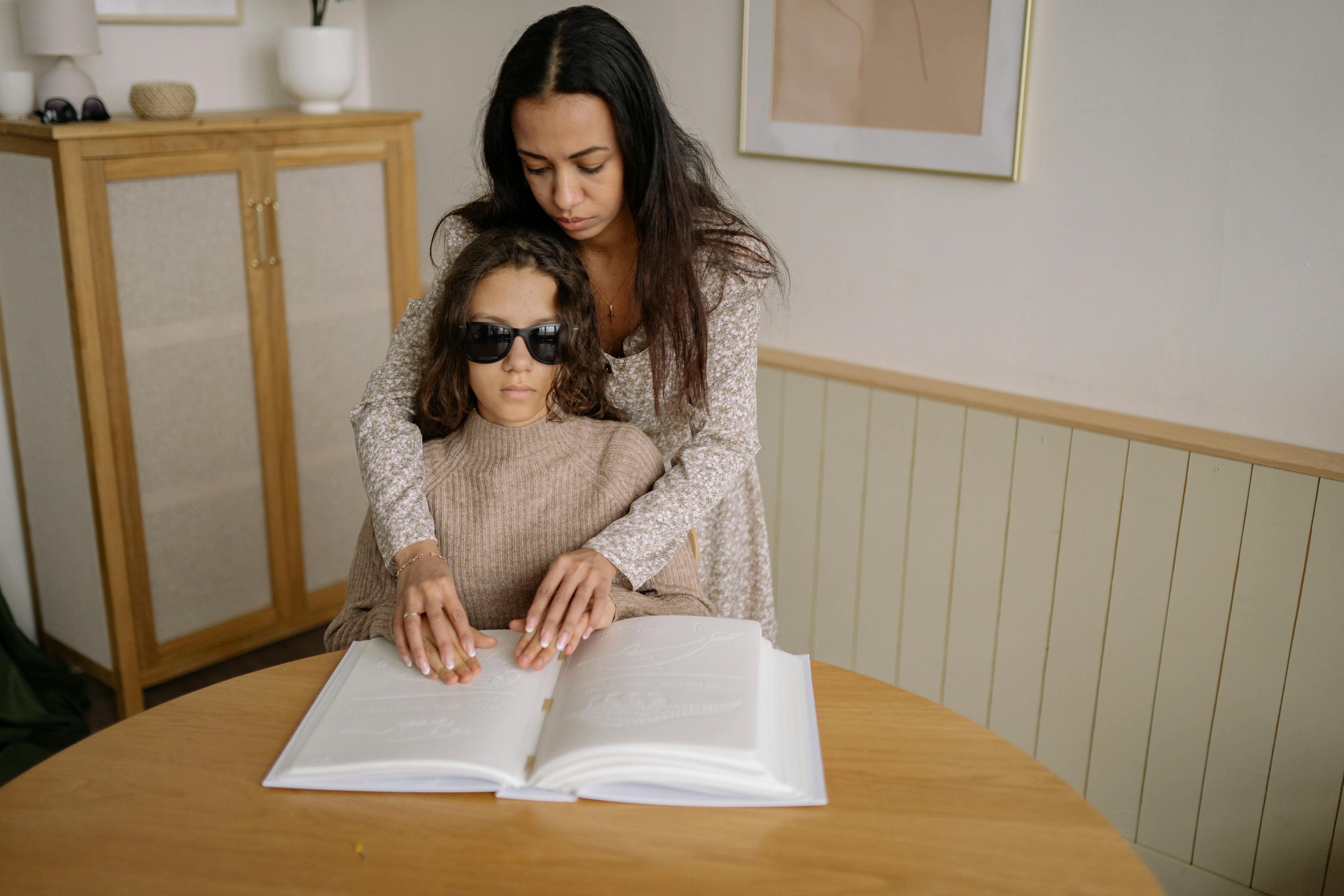 Mãe auxilia filha a ler livro em Braille